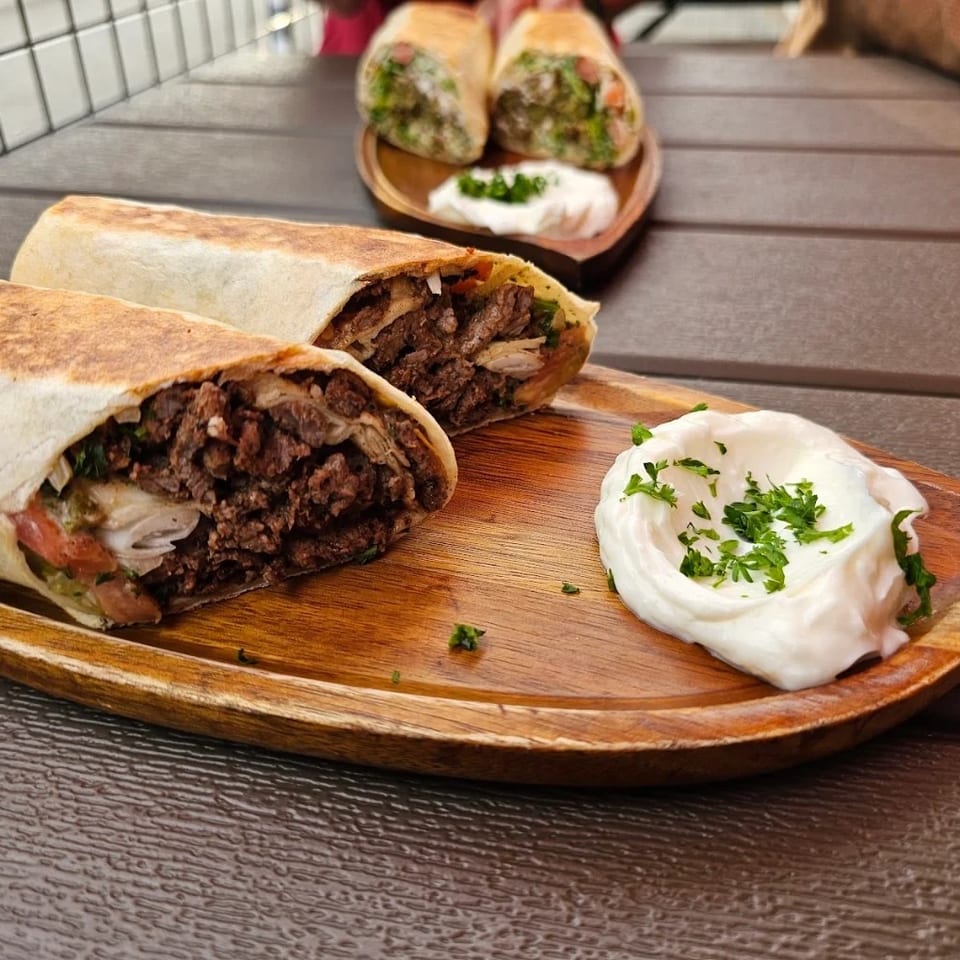 Two beef shawarma wraps with white sauce and parsley on a wooden platter.