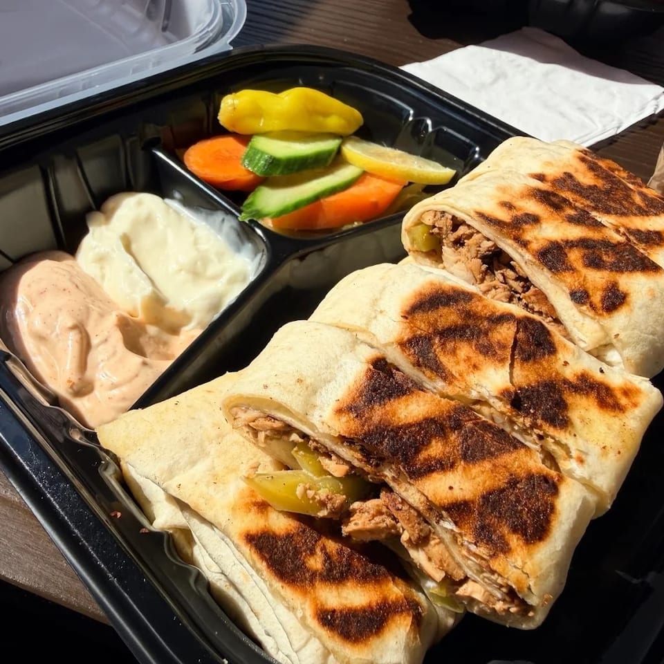 Shawarma wraps with sauces and pickled vegetables in a black takeout container.