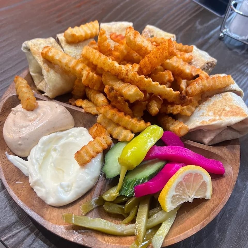Shawarma wraps, crinkle-cut fries, two dips, and pickled vegetables on a wooden plate.