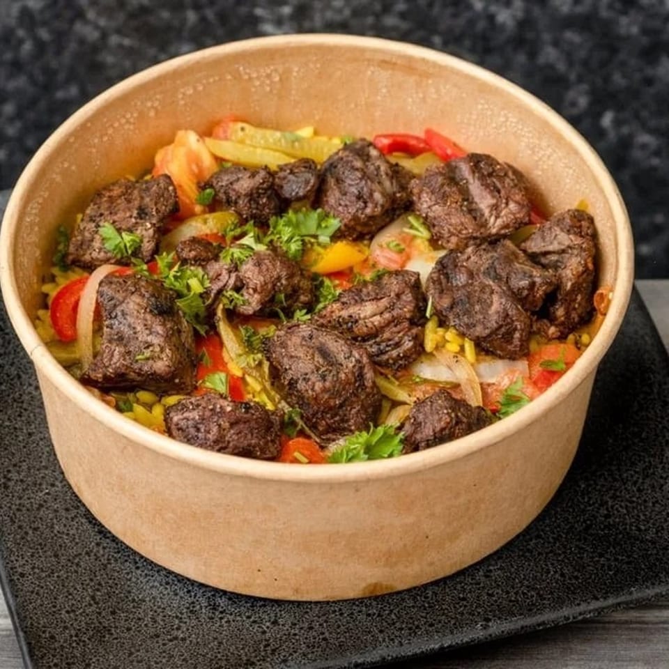 Savory beef and vegetable stir-fry in a brown paper bowl on a black plate.